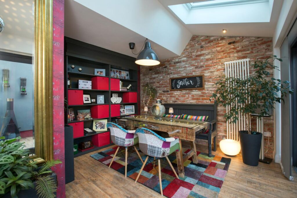 This bright yet cosily furnished dining area is new; the couple love to upcycle and the old bricks, which are from Poland, are sliced in half and treated so that they adhere easily to the walls. The floor is covered in wood-effect tiles. The bookshelves conceal sliding doors to the den.The dining table is an old workbench covered with custom-made glass